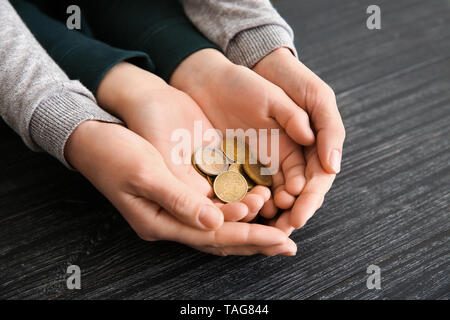 Le mani della donna e suo figlio holding monete sul tavolo di legno. Concetto di supporto per il bambino Foto Stock