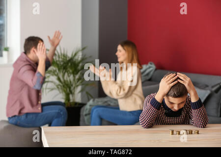 Triste ragazzino con monete e il suo quarreling genitori a casa. Concetto di supporto per il bambino Foto Stock