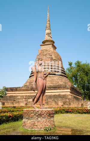 La scultura di un Buddha a piedi contro lo sfondo di una stupa medievale. Le rovine di un tempio buddista nel parco storico di Sukhothai sità. Thail Foto Stock