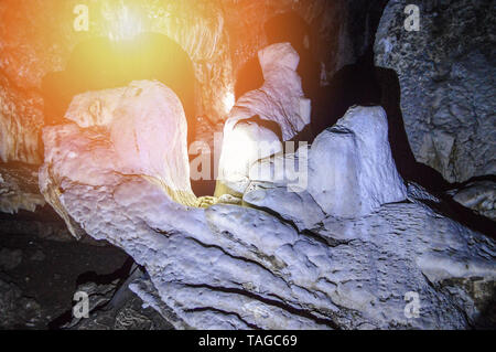 Stalagmiti e stalattiti in pietra oscura grotta con la luce dalla torcia elettrica Foto Stock