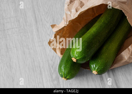 Zucchina organico in un sacchetto di carta su legno grigio. Riciclare la confezione del concetto. No dei rifiuti di plastica. Foto Stock