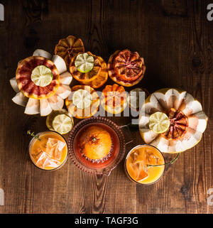 Vari colorati agrumi con spremuta fresca di succo di agrumi in bicchieri con cubetti di ghiaccio sul tavolo con ingredienti: arancio, limone, pompelmo, manda Foto Stock