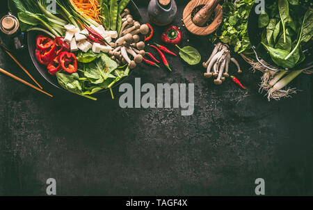 Cibo asiatico dello sfondo. Padella wok con ingredienti vegetariano: verdure e tofu sul tavolo da cucina con bacchette, erbe aromatiche e spezie, vista dall'alto. Copia spa Foto Stock