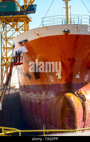 La pulizia e la riverniciatura degli scafi di una grande nave o grande nave essendo fissato in un cantiere o grande nave da riparare e dipinta in un bacino a secco o la nave Foto Stock