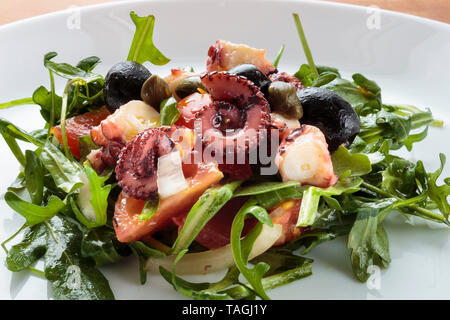 Insalata di polipo con rucola e olive su piastra bianca Foto Stock