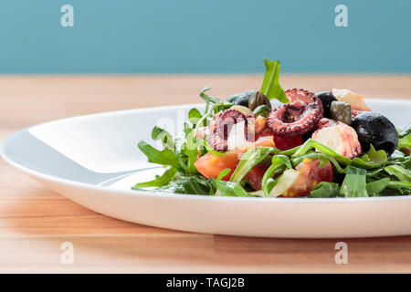 Insalata di polipo con rucola e olive su piastra bianca con sfondo blu Foto Stock