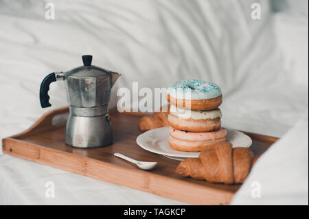 Pila di ciambelle vetrata con croissant e caffè turk sul vassoio in legno a letto. Buona mattina. Una gustosa prima colazione. Messa a fuoco selettiva. Foto Stock