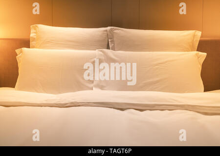 Fogli bianchi di letto king size con doppio di cuscini e una luce calda Foto Stock