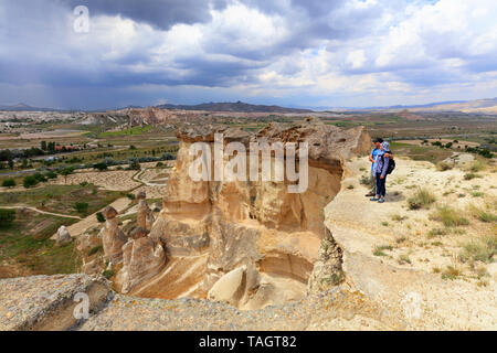 Una giovane coppia di turisti con zaini sulle loro spalle sorge sul bordo di una scogliera in Cappadocia e ammira lo spazio circostante contro la BAC Foto Stock