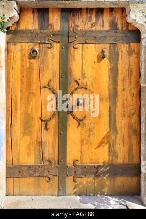 Antique le porte in legno massiccio con maniglie battuto, rivetti e traverse illuminata da un sole luminoso. Foto Stock