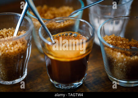 Schiumoso caffè espresso in tazza di vetro con cucchiaio in metallo e zucchero Foto Stock