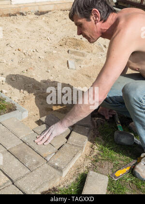 Lavoratore mette i blocchi, la creazione di un marciapiede, per la costruzione di un patio e una via nel cortile di una casa privata Foto Stock