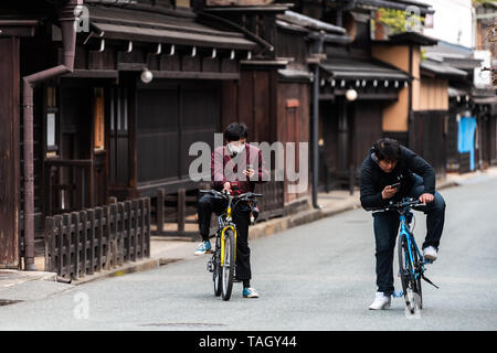 Takayama, Giappone - Aprile 6, 2019: Prefettura di Gifu in Giappone con le tradizionali case di legno sul vicolo strada e persone giovani uomini su biciclette cercando Foto Stock