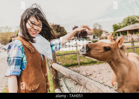 Ritratto di una bella donna cinese cowgirl mentre accarezzare un puledro nel suo recinto Foto Stock