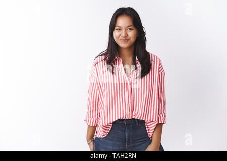 Divertente e divertito carina ragazza cercando nascondi ridere come ridacchiando e sorridente felicemente, ponendo upbeat contro uno sfondo bianco in camicia a righe e jeans Foto Stock