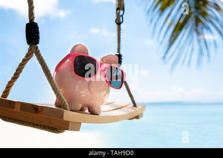 Close-up di Rosa Piggybank con gli occhiali da sole sul brandeggio in legno a Beach Foto Stock