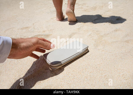 Close-up di un uomo prendendo donna portamonete perduto sulla sabbia in spiaggia Foto Stock