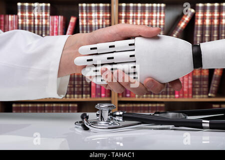 Close-up del medico e il robot si stringono la mano su uno stetoscopio in clinica Foto Stock