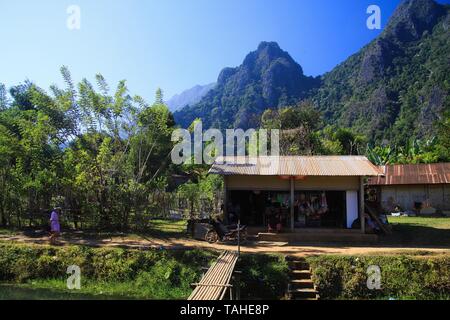 VANG VIENG, LAOS - Dicembre 22. 2017: Casa shop nel paesaggio rurale con montagne carsiche e bridge - Vang Vieng, Laos Foto Stock