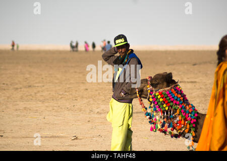 Rann di Kutch, Gujarat, India - circa 2018 : proprietario del cammello herder in piedi con la sua decorato in maniera colorata cammello seduto per terra. Questi cammelli dare Foto Stock