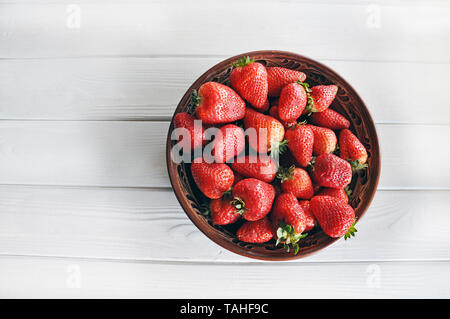 Ripe rosso Fragole sulla tradizionale piatto di argilla sul bianco tavolo in legno, vista dall'alto Foto Stock