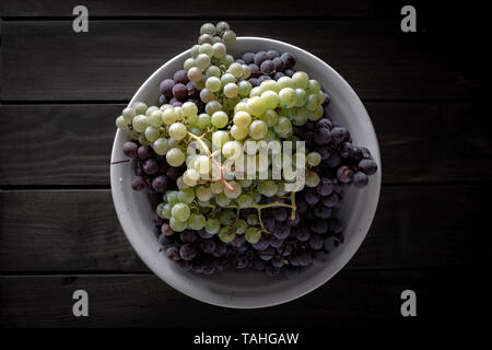 Vista superiore del rosso fresco e uve bianche in bianco ciotola sul tavolo di legno. Dark food style Foto Stock
