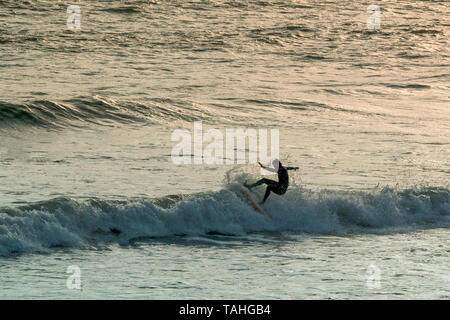 Surfista che esegue una manovra su un'onda di rottura al tramonto, Rest Bay, Porthcawl, Galles, Regno Unito. Foto Stock