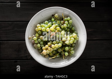 Vista superiore della fresca Uva bianca in bianco ciotola sul tavolo di legno. Dark food style Foto Stock