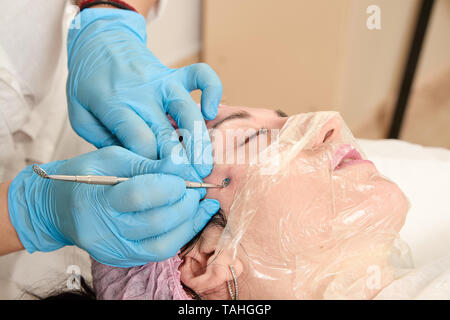 Giovane donna nel salone di bellezza non faccia manuale di pulizia. Rimozione manuale di brufolo, acne, blackhead, furuncle purulento sulla faccia. Medico e di bellezza eq Foto Stock