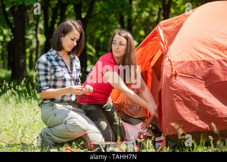 Le femmine durante il campeggio vicino a tenda con piatti. Erba verde foresta e sul background. Foto Stock