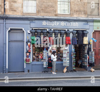 Una giovane donna controllando il suo telefono esterno semplicemente scozzese, un negozio di souvenir scozzese, nel Royal Mile / High Street nella città vecchia di Edinbu Foto Stock