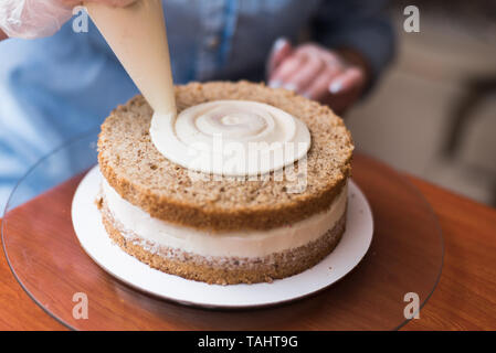 Ragazza pasticcere, fa una torta di nozze con le proprie mani e spreme la crema sulla torta a strati. Copia dello spazio. Messa a fuoco selettiva. Foto Stock