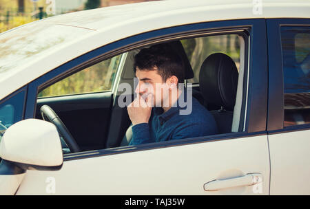 Considerato giovane conducente la mano sotto il mento cercando ansiosa attesa in sua automobile. Triste ragazzo serio bloccato nel traffico. Foto Stock