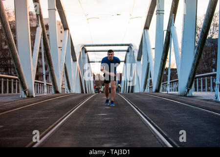 Uomo che corre runner facendo formazione outdoor city eseguire in volata su un ponte. Urban un sano stile di vita attivo. Atleta maschio in esecuzione su sunset backgroun Foto Stock