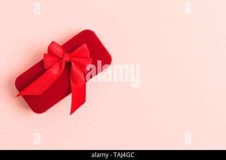 Red gioielli confezione regalo con prua tessili su sfondo rosa con copia spazio. Lay piatto. Concetto di vacanza. Presente in occasione di feste di compleanno, il giorno di San Valentino o woma Foto Stock