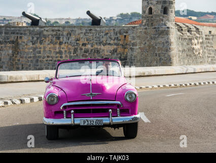 L'Avana, Cuba - un taxi passa nella parte anteriore del Castillo de San Salvador de la punta sul Malecón road di fronte Baia dell Avana. Classic American cars dal 19 Foto Stock