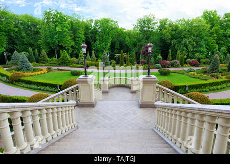 Elegante scalinata in granito con una balaustra con belle ringhiere intagliate in stile classico, si affaccia sul bellissimo prato verde di un magnifico giardino. Foto Stock