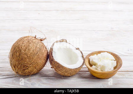 Sfondo di cocco, di guscio di noce di cocco, olio duro nella ciotola di legno bianco sul tavolo di legno Foto Stock