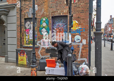 Londra SPITALFIELDS Brick Lane e PRINCELET STREET CON WALL ART GRAFFITI E UOMO ricerca attraverso la spazzatura Foto Stock