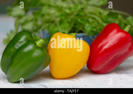 Tre peperoni rosso, giallo e verde con il coriandolo in background Foto Stock