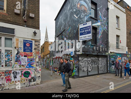 Londra SPITALFIELDS Brick Lane passanti con arte e graffiti sui muri di casa Foto Stock