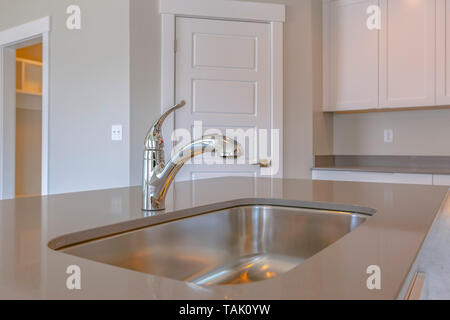 Shiny lavello in acciaio inox e il rubinetto sul bancone all'interno di una cucina. Montato a parete Armadi e porte può essere visto anche su questa stanza. Foto Stock