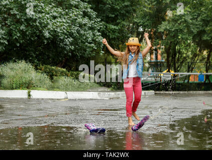 Happy funny bambina saltando su pozzanghere in stivali di gomma e ridere. Foto Stock
