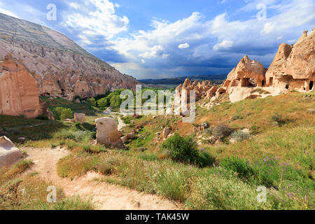 La sporcizia country road e antiche a forma di cono picchi di rocce, luminose verdi vallate con aranceti sullo sfondo di un paesaggio di montagna con un Foto Stock