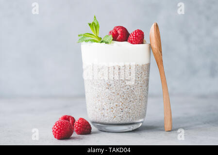 Budino di Chia parfait con yogurt e lamponi in un bicchiere. Di cemento grigio Sfondo texture Foto Stock
