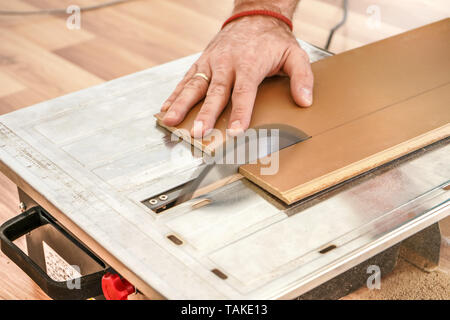 Uomo taglio pavimento laminato schede su una sega circolare, dettaglio sulle mani tenendo il pannello di legno Foto Stock