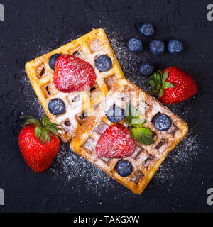 In casa tradizionale cialde belghe con frutta fresca, frutti di bosco e zucchero in polvere sulla piastra nera. Appartamento laico, vista dall'alto, copia dello spazio. Foto Stock