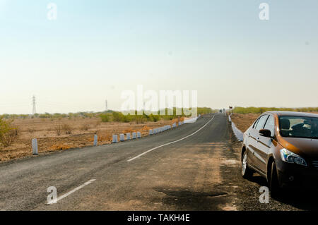 Gujarat, India - circa 2018: Shot che mostra un marrone sedan auto parcheggiate sul lato della strada con un vuoto di una singola corsia strada che tratti di in Foto Stock