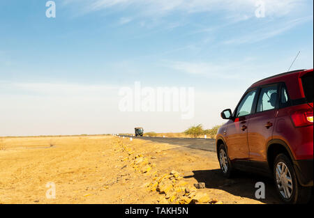 Gujarat, India - circa 2018: Shot che mostra auto rossa su un lungo tratto di autostrada vuota nel Rann di Kutch Gujarat. Il giallo sabbia e bella blu clou Foto Stock