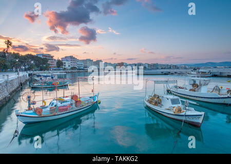 Sunrise colorato lungo il lungomare e il porto di Loutraki, Grecia. Cielo dipinto su barche da pesca ormeggiate presso il dock in questa città turistica. Foto Stock